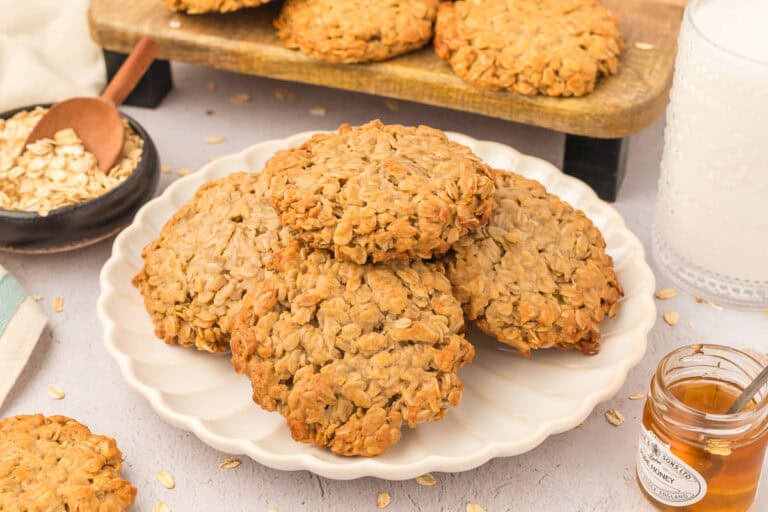 3 ingredient oatmeal cookies stacked on a white plate with oats, honey and milk around