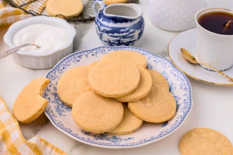 3 ingredient shortbread cookies stacked on a plate with a cup of coffee in the background