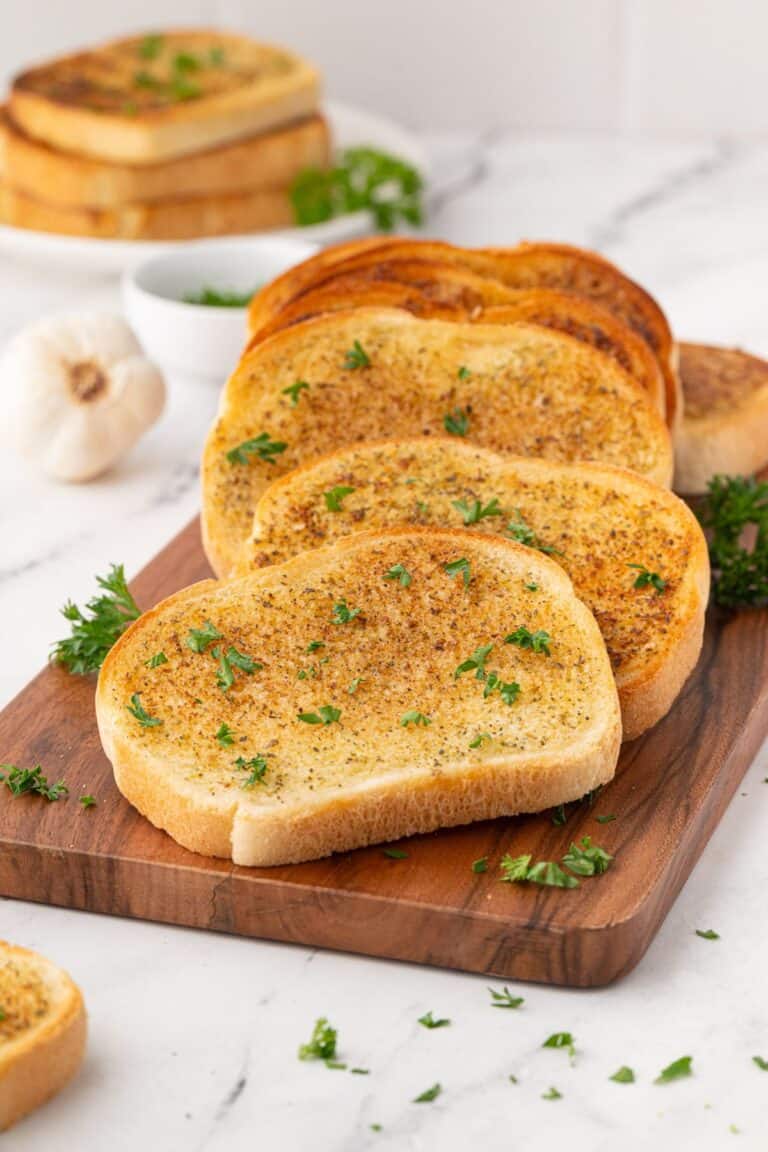 Rustic wooden board with freshly toasted garlic bread, garnished with parsley.
