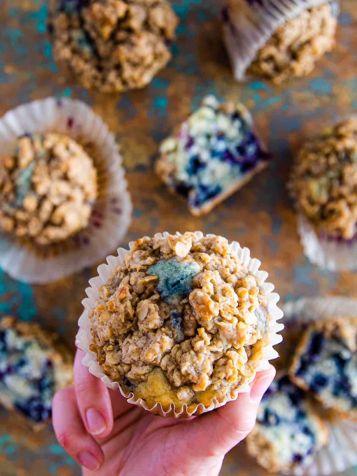 A single blueberry buttermilk muffin held up, emphasizing its homemade, bakery-style appeal with the oat streusel topping.