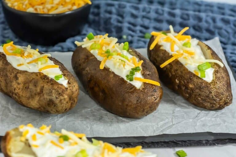 slow cooker baked potatoes lined up on a serving plater split open with butter, sour cream, cheese and chives